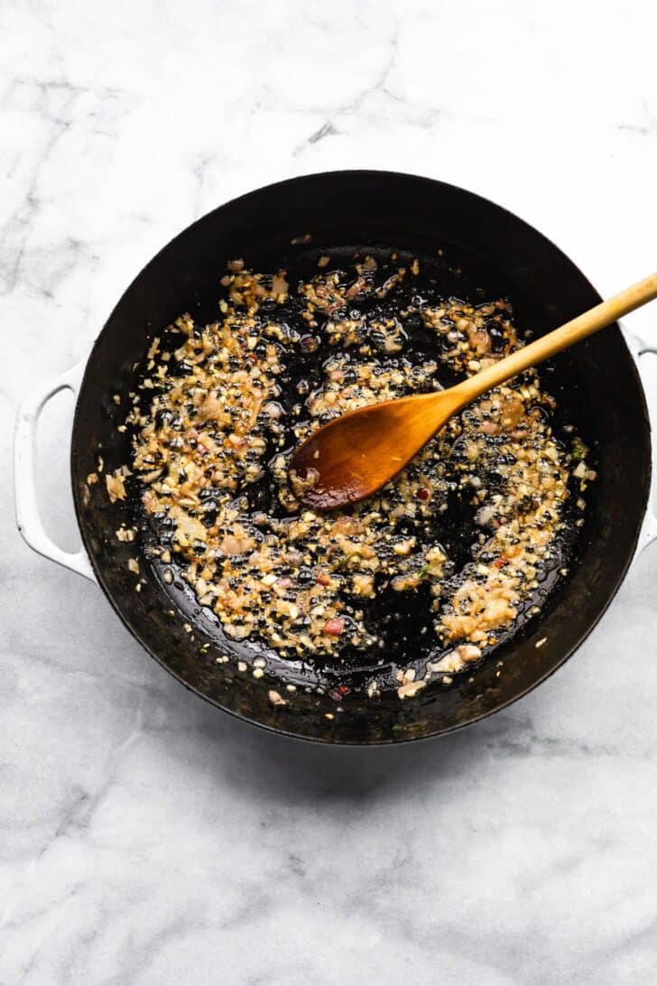 Onions and garlic sautéing in cast iron skillet with wooden spoon