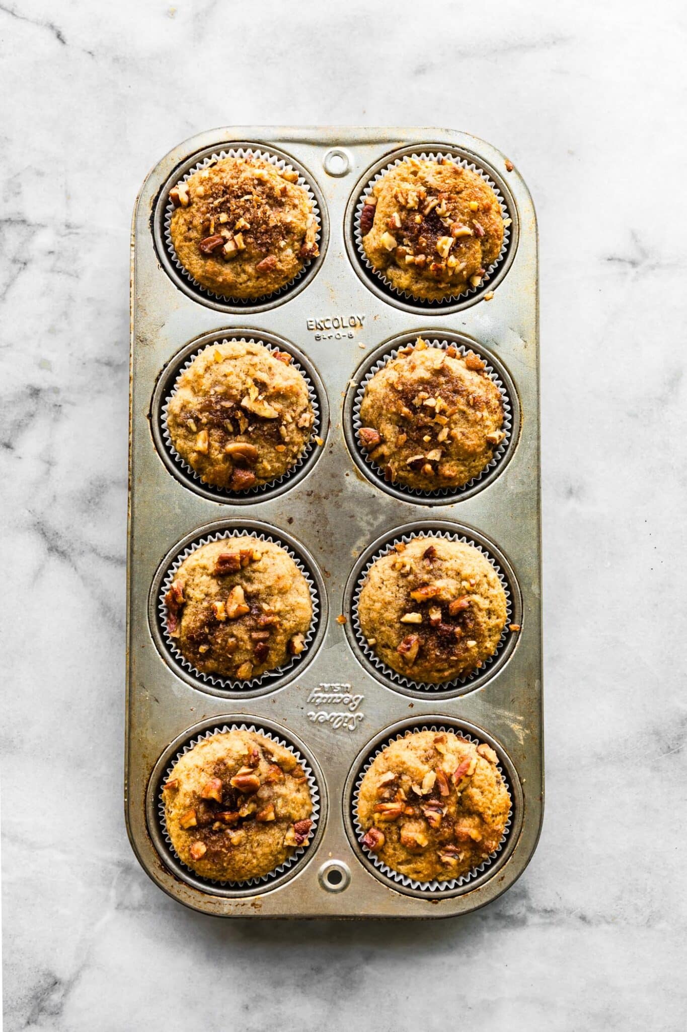 Eight baked banana muffins topped with chopped nuts in a muffin pan.