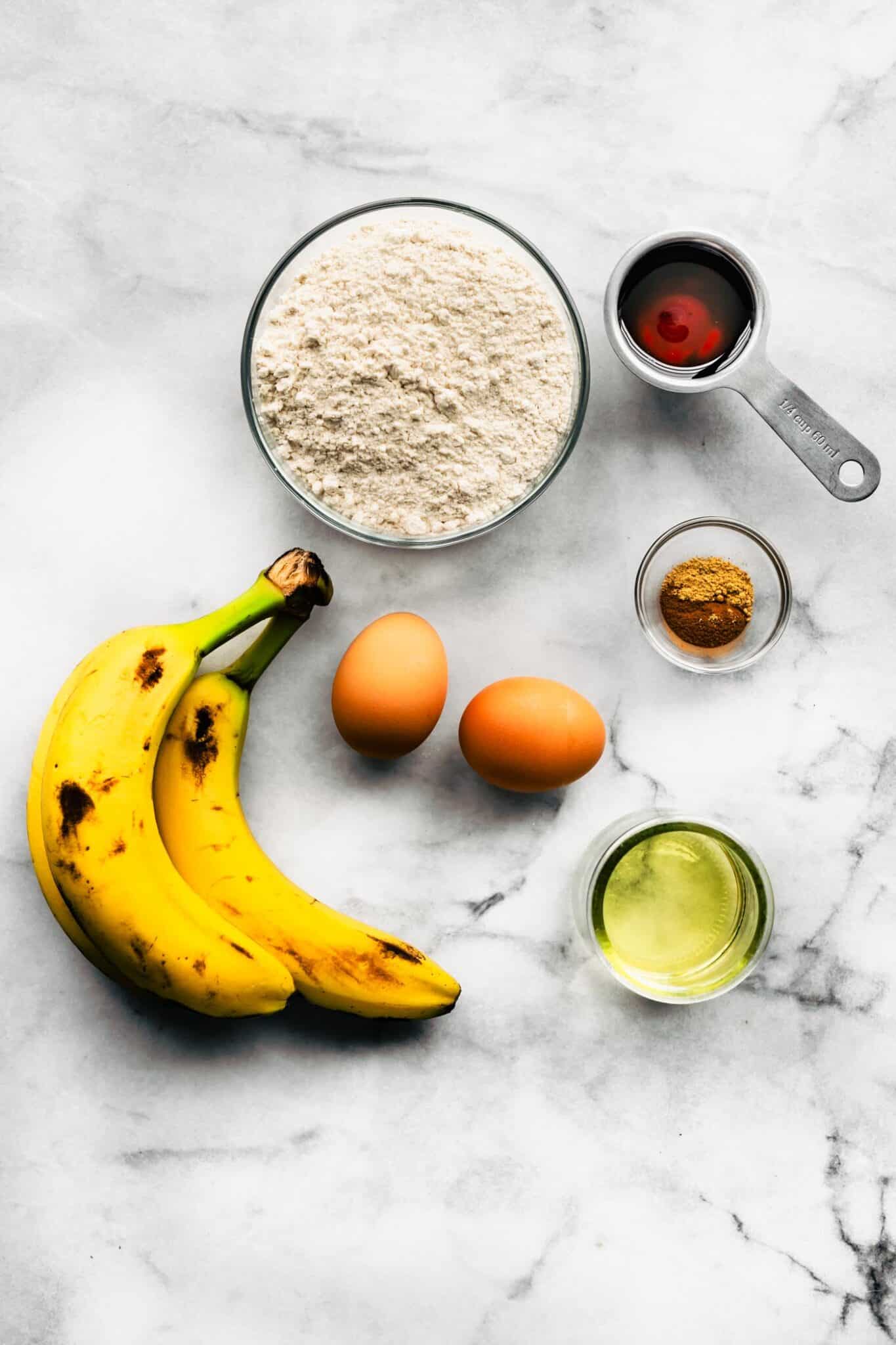 Ingredients for banana muffins on a white marble countertop.