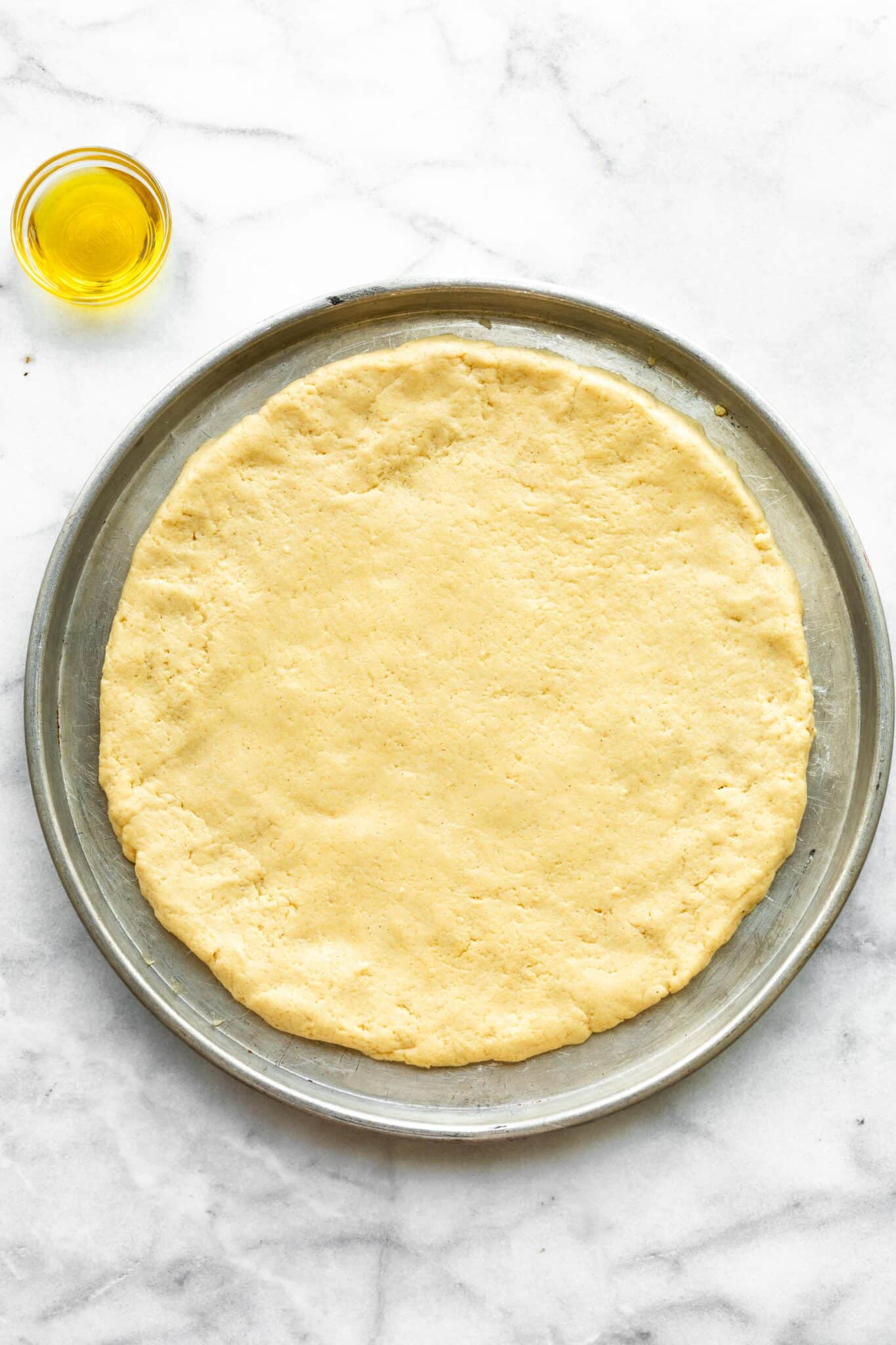 No yeast pizza dough rolled out on a metal pan with a jar of oil.