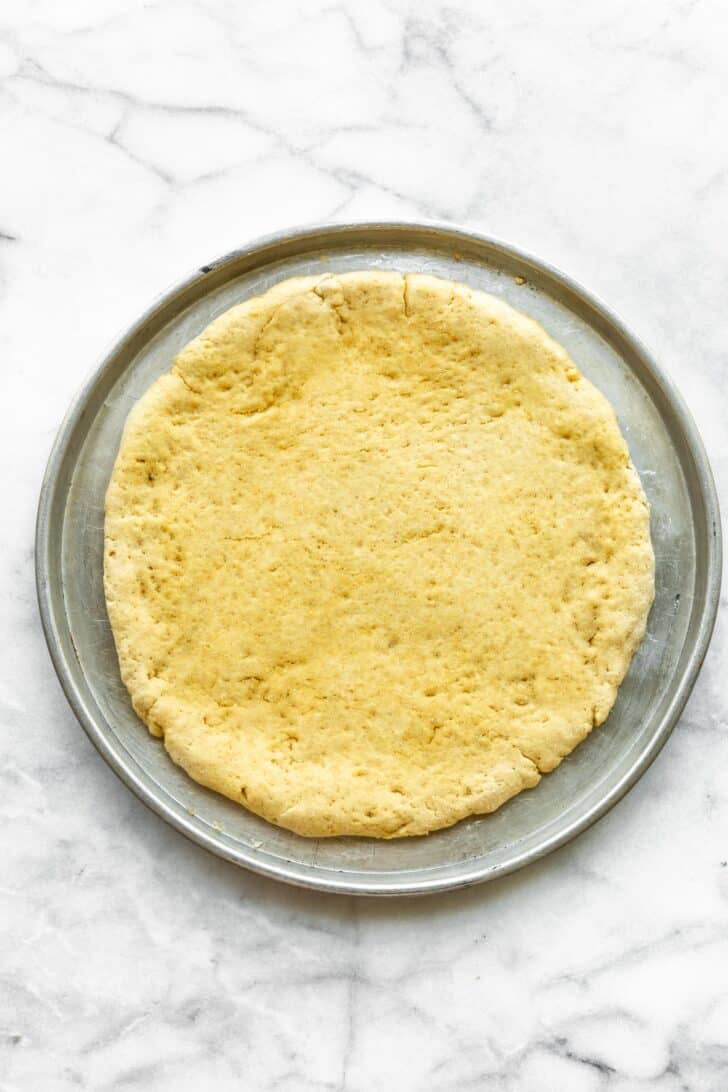 Overhead photo of gluten free pizza dough on a round metal pan.