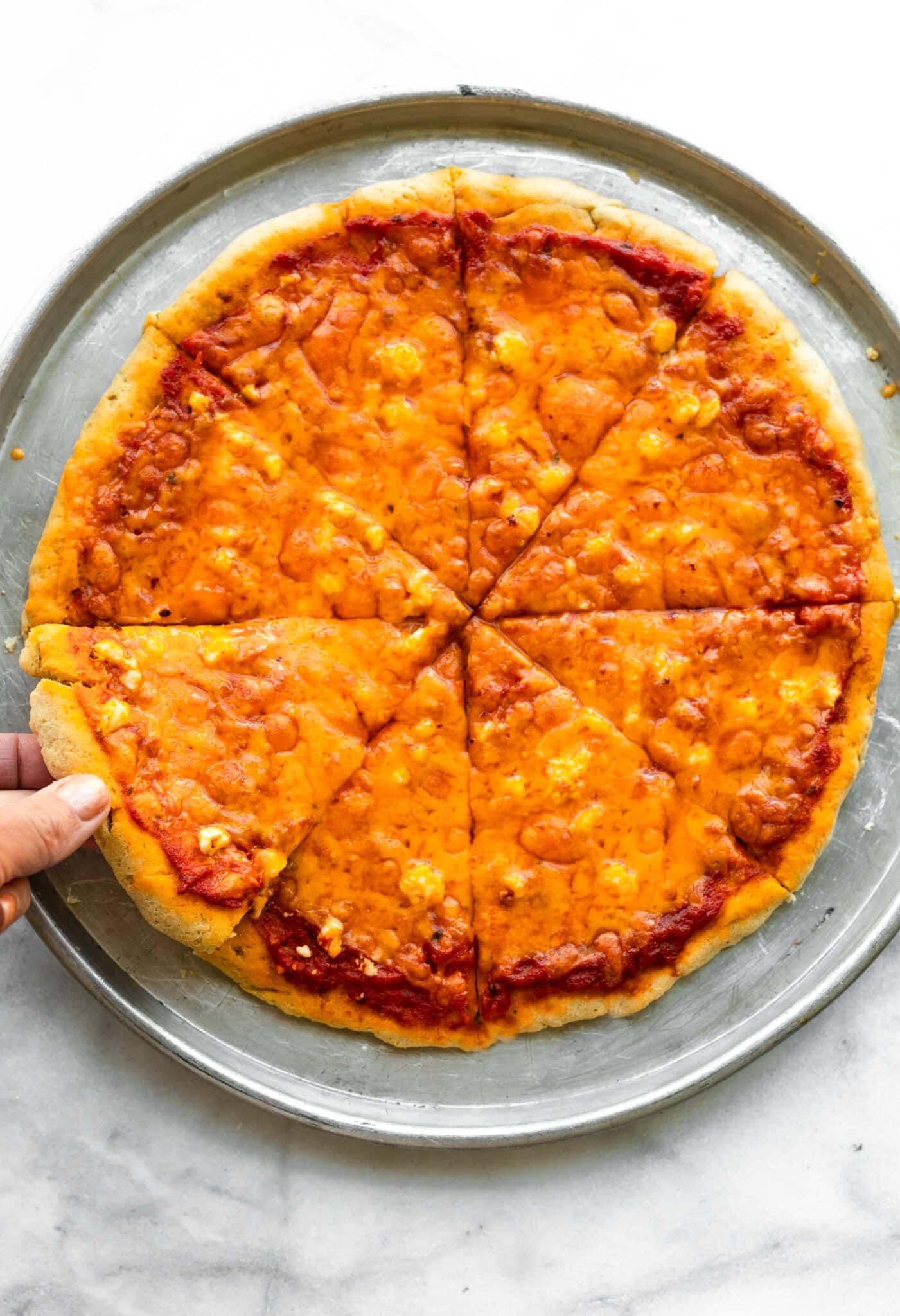 Overhead photo of a woman's hand picking up a slice of cheese pizza.