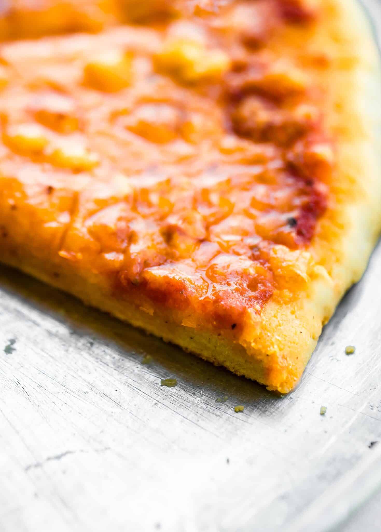 Up close photo of a slice of cheese pizza on a metal pizza pan.