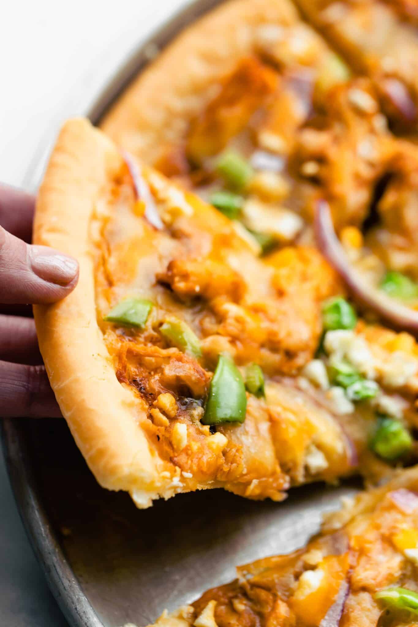 Up close photo of a woman holding up a slice of BBQ chicken pizza.