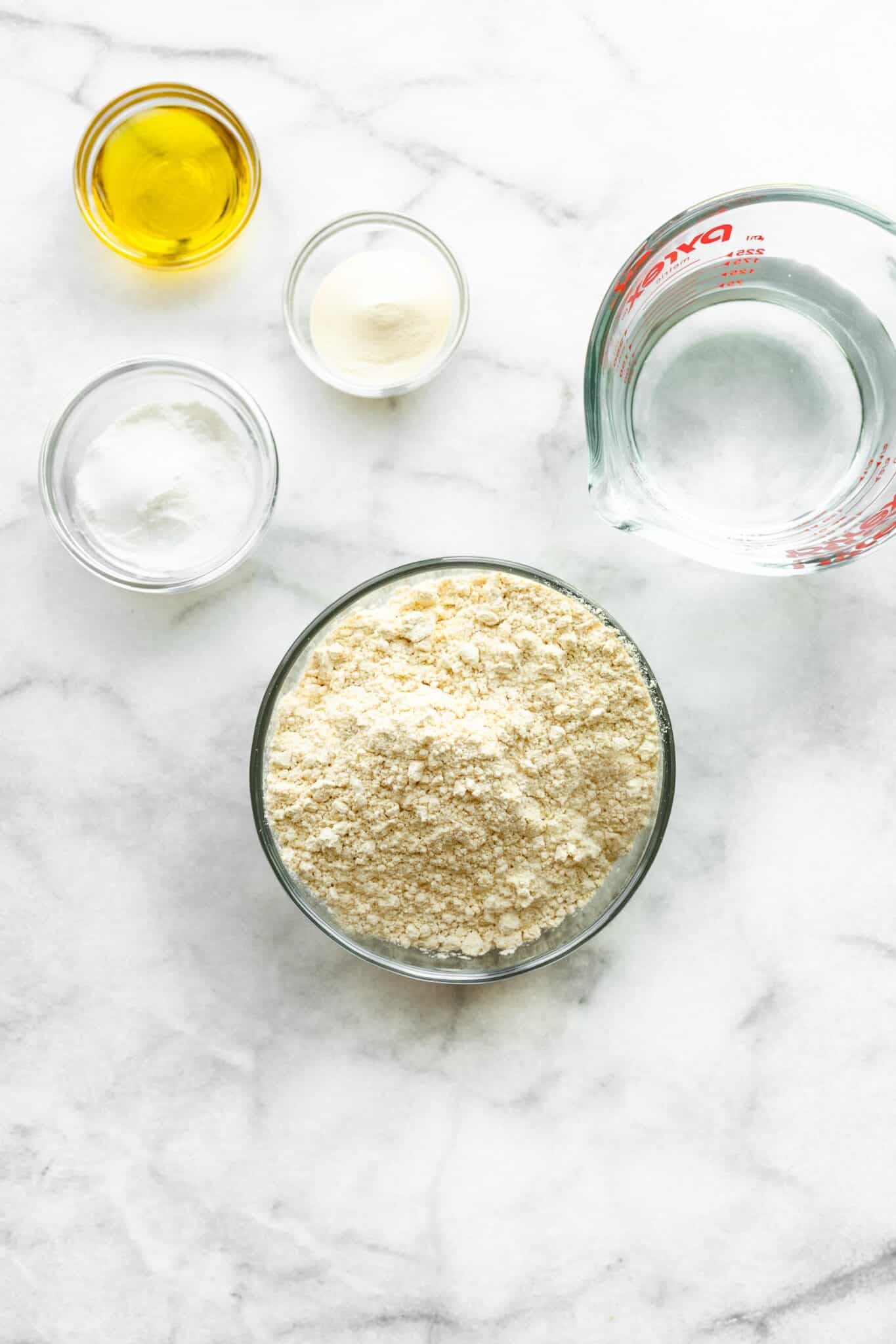 Ingredients for no yeast pizza crust on a white marble countertop.