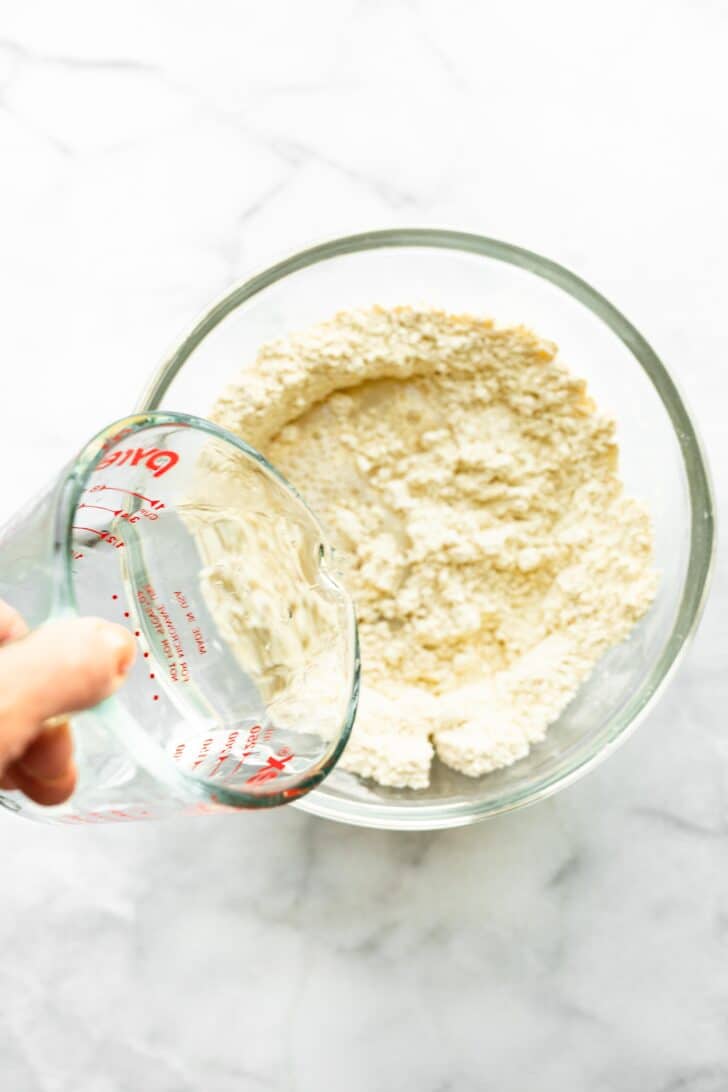 Pouring water into a gluten free flour mix in a glass bowl.