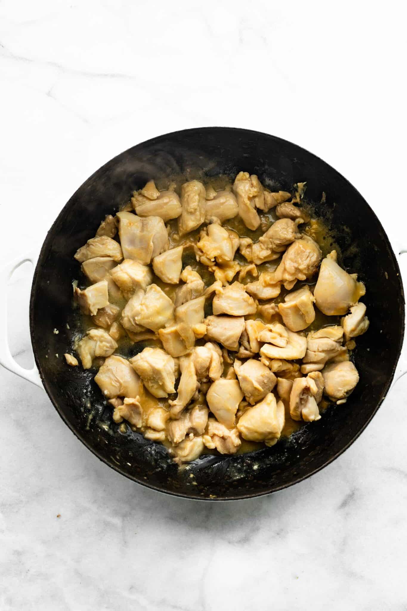 Overhead photo of chopped chicken thighs browning a pan.
