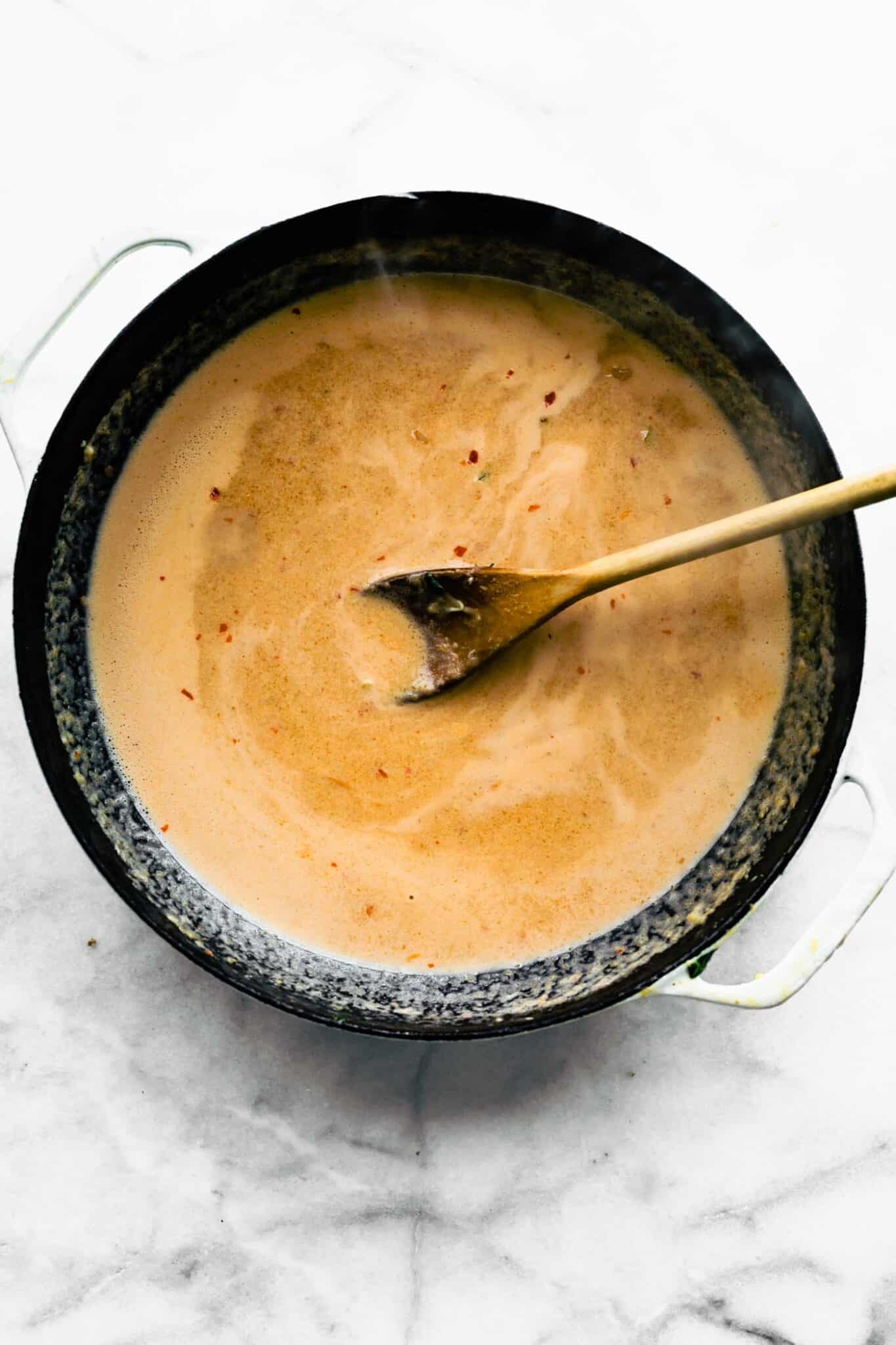 Overhead photo of a wooden spoon stirring a pan of Thai peanut noodle sauce.