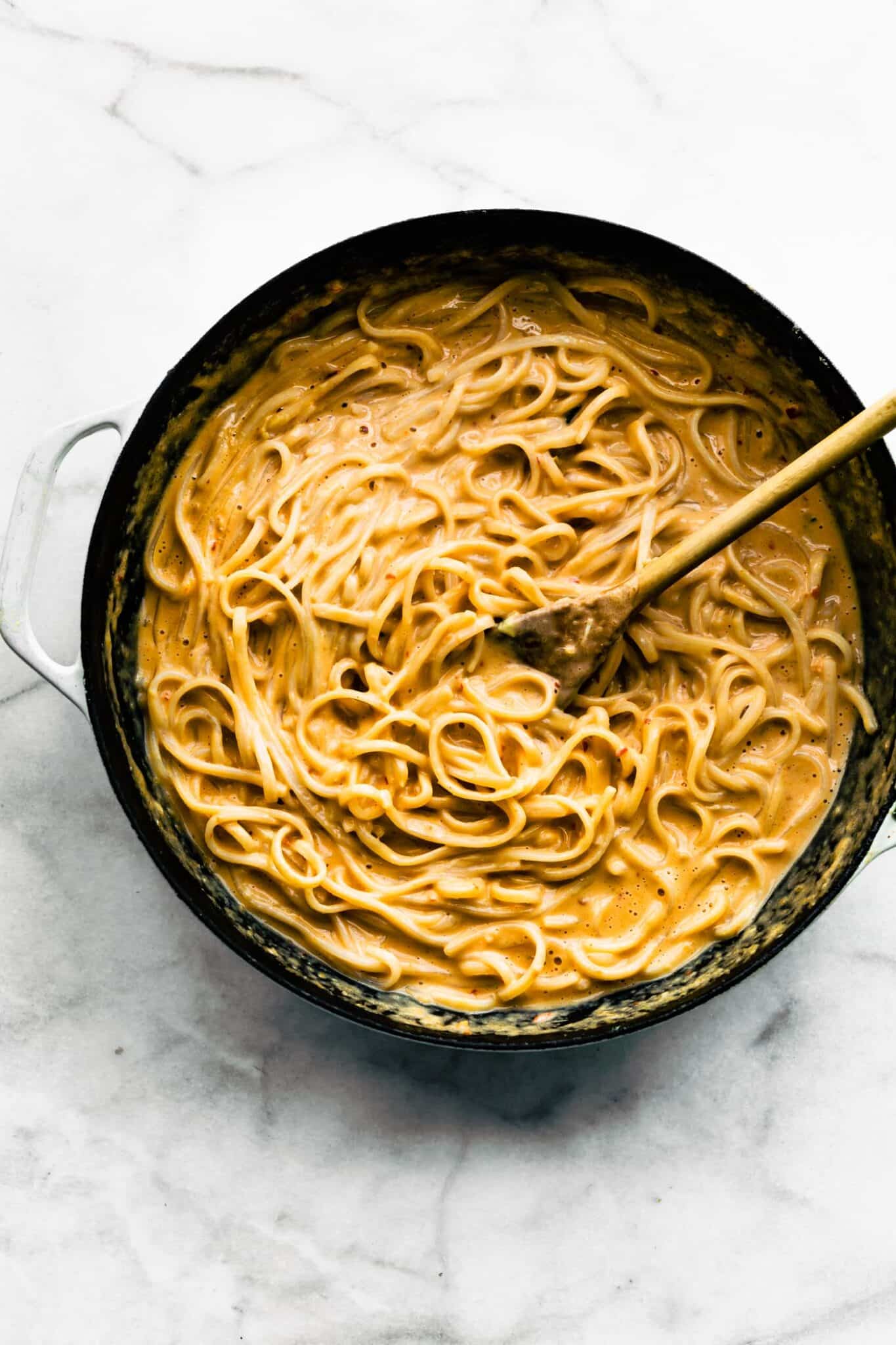 Overhead photo of rice noodles in a creamy Thai peanut sauce with a wooden spoon.