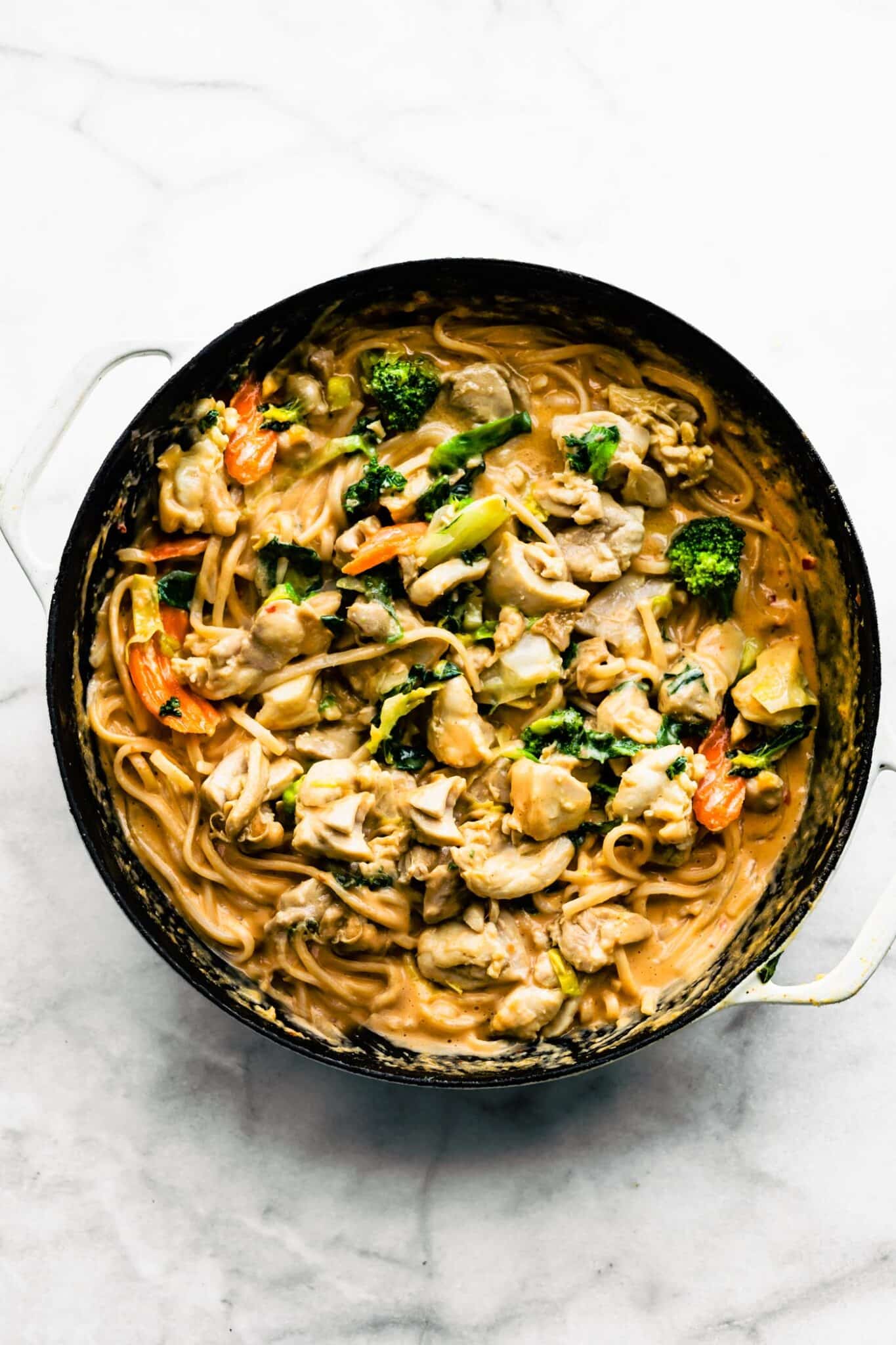 Overhead photo of rice noodles and veggies in a peanut sauce in the pan.