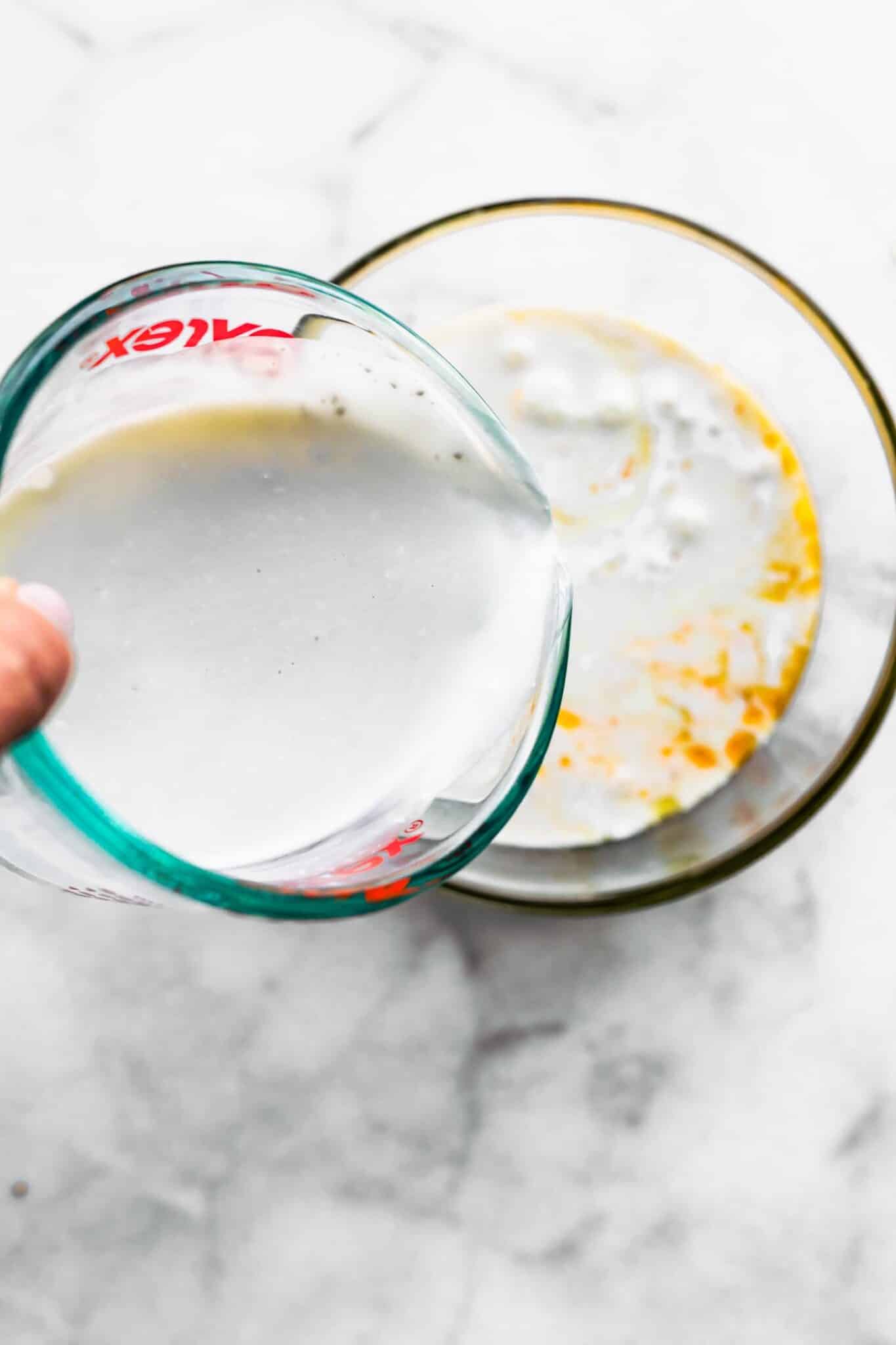 Coconut milk being poured into a glass mixing bowl.
