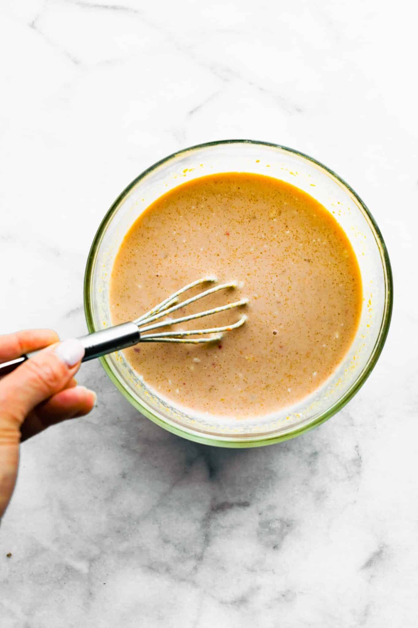 A woman's hand using a small whisk to combine peanut butter and coconut milk.