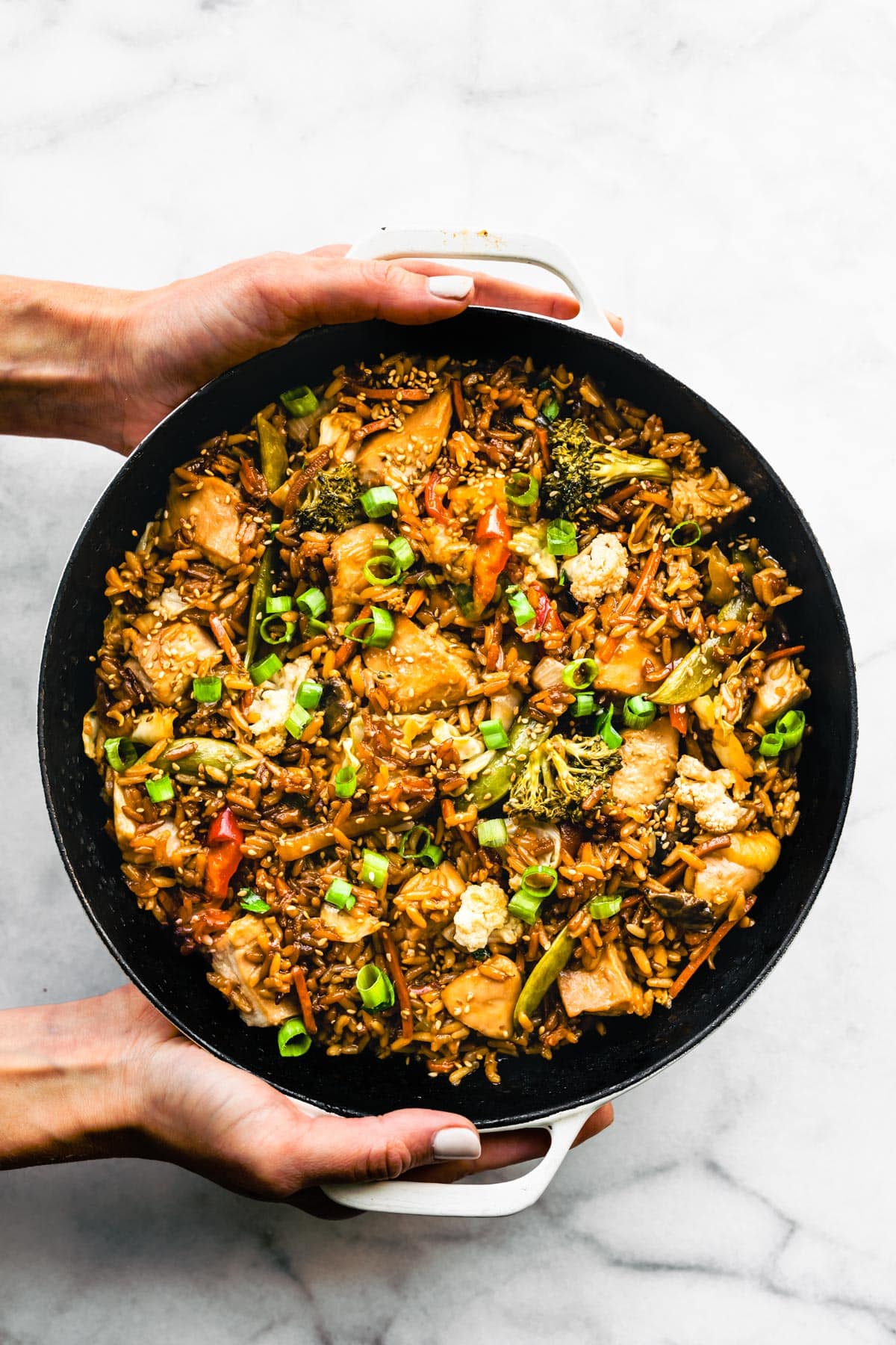 Two woman's hands holding gluten free teriyaki chicken casserole.