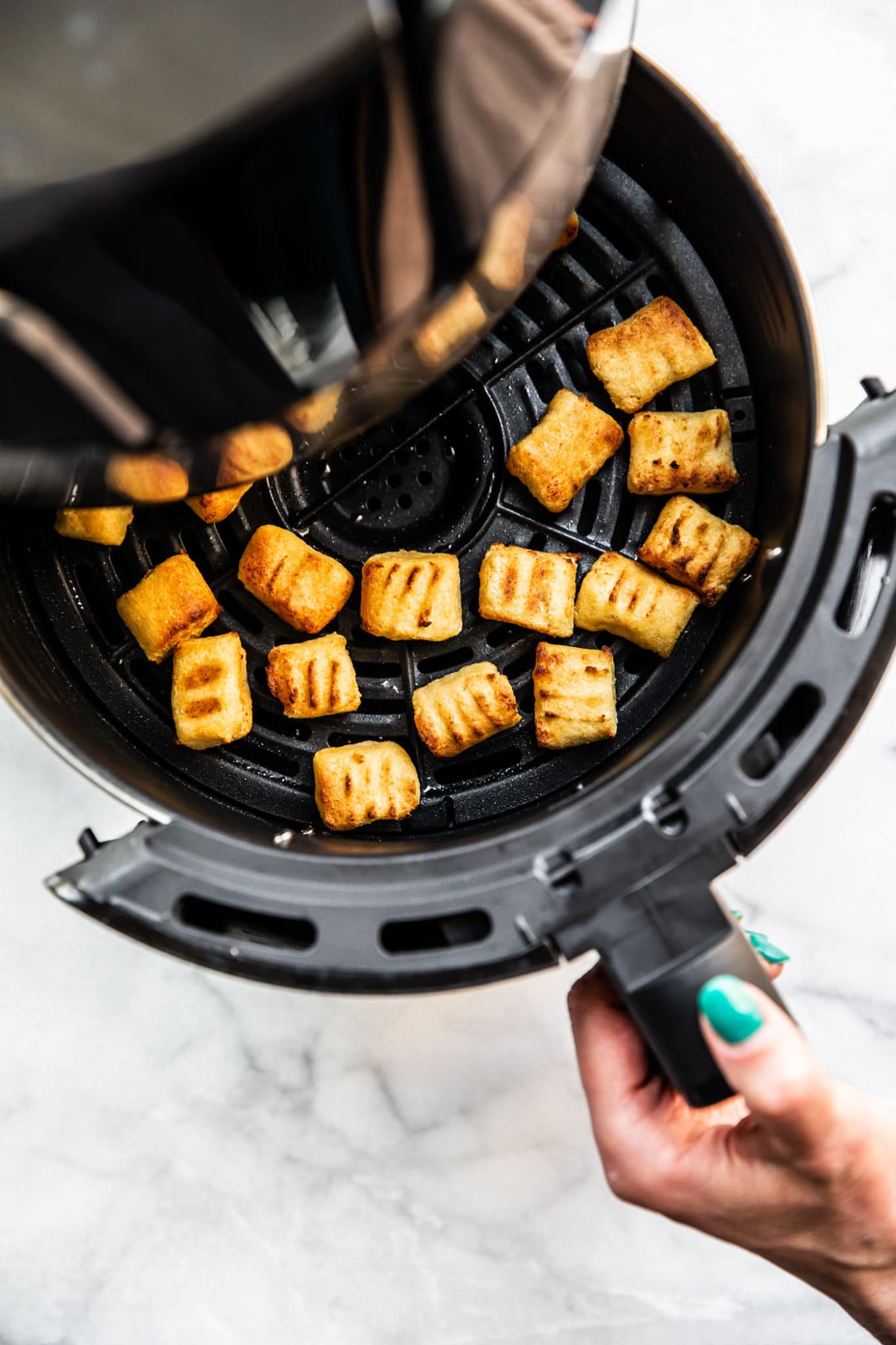Air fried gnocchi in a black air fryer basket.