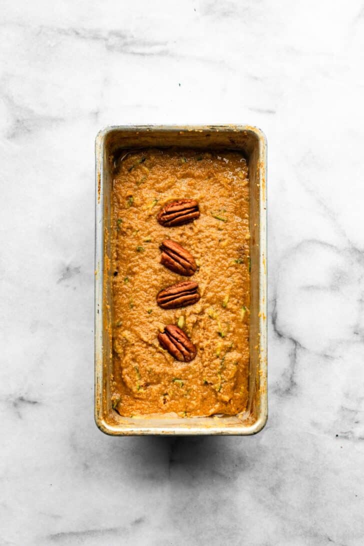overhead photo of unbaked zucchini bread batter with walnuts in a baking pan