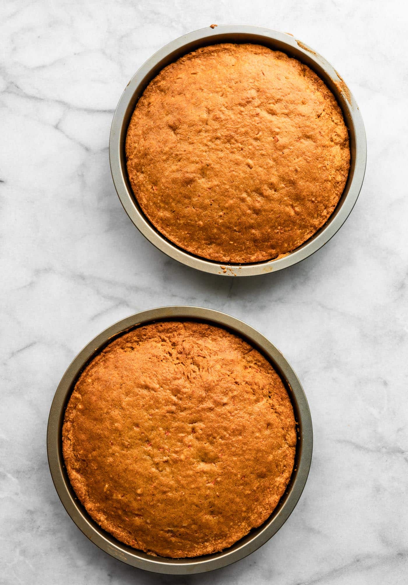 Two golden brown baked carrot cakes in round cake pans.