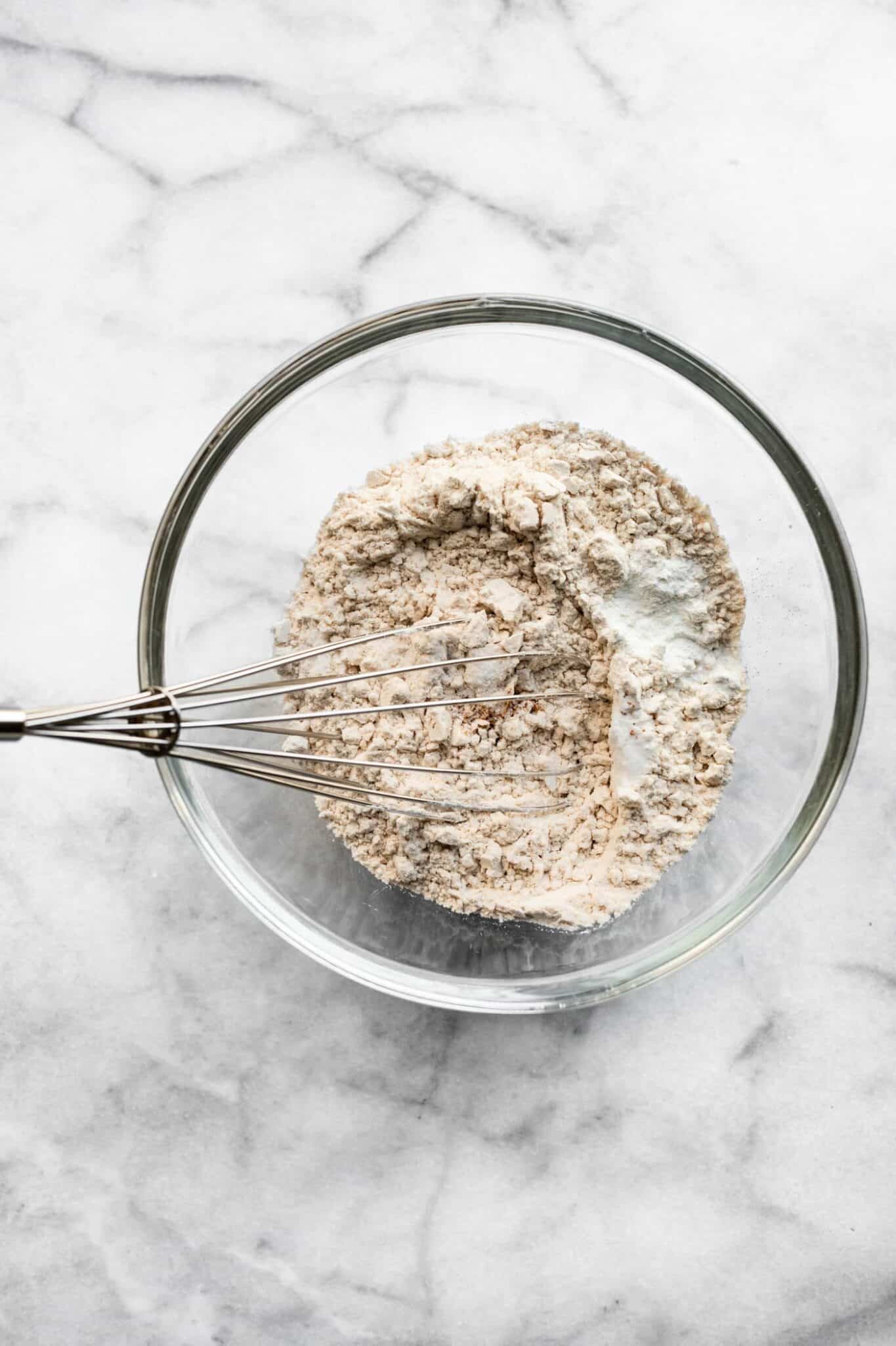 A metal whisk mixing dry ingredients in a glass bowl.