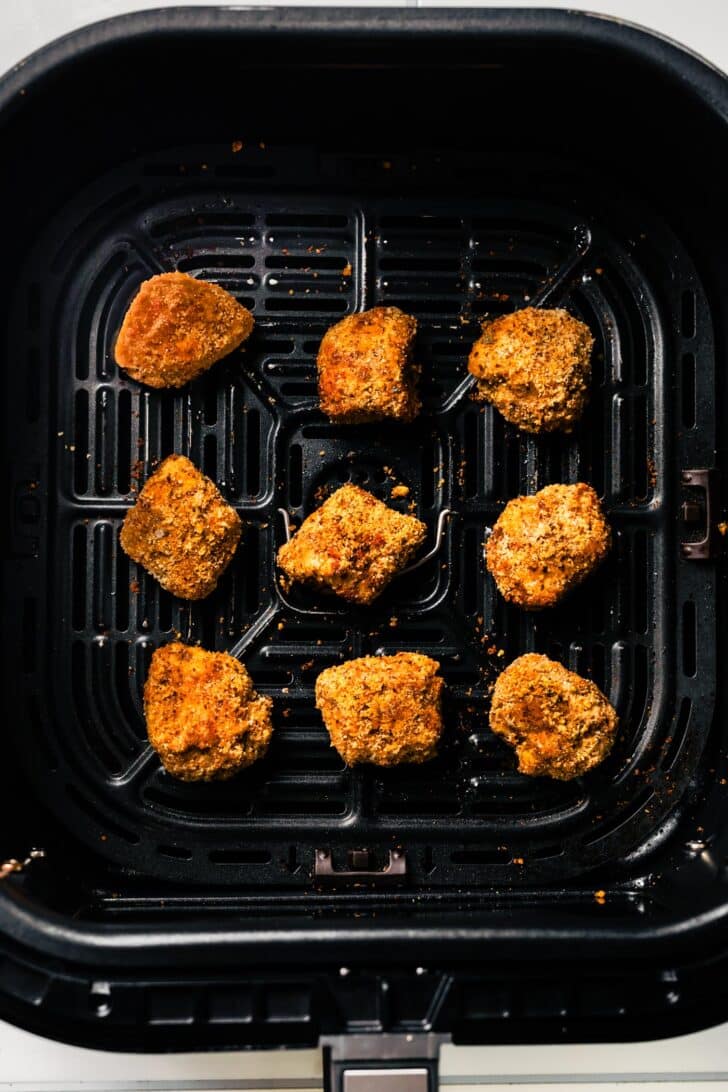 Breaded chicken nuggets in an air fryer basket after cooking, edges crispy and brown