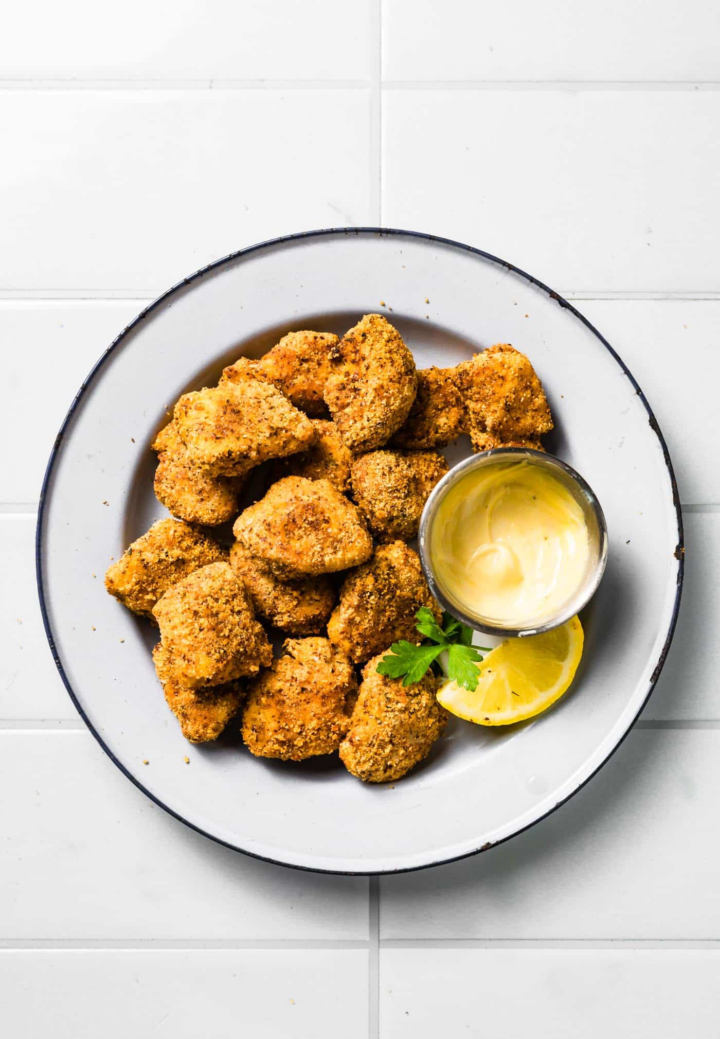 Finished gluten-free chicken nuggets on a white plate with a small dipping bowl of sauce, lemon wedge, and parsley garnish.
