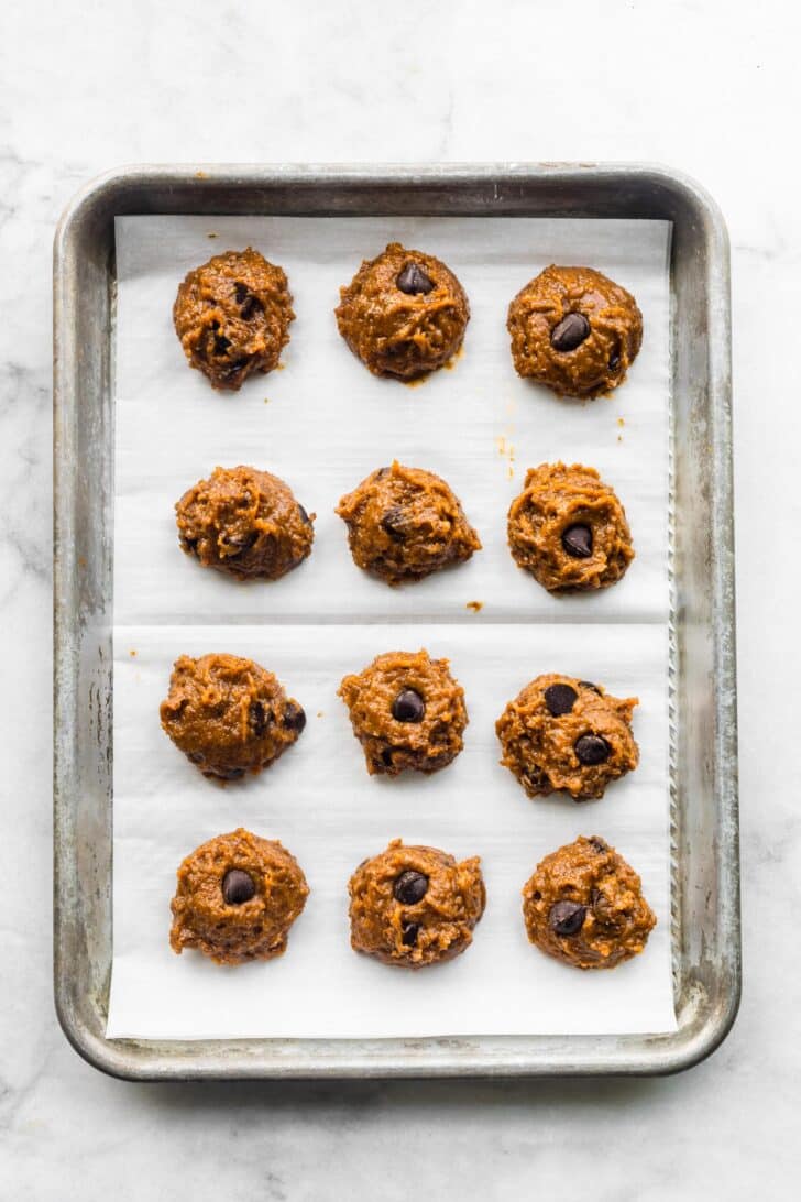 Pumpkin chocolate chip cookie dough scooped into mounds on a parchment-lined baking sheet, ready to bake.