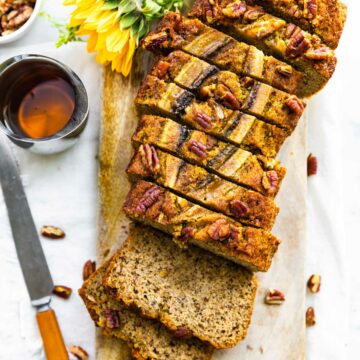 overhead photo: loaf of low carb banana bread cut into slices on wooden board next to knife and honey