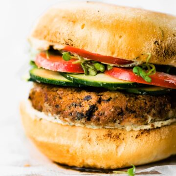 a vegan greek quinoa burger on a gluten free bun with tzatziki, cucumbers, tomatoes, and fresh herbs