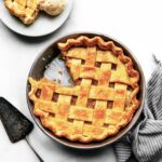 Apricot pie with a slice removed and served on a plate with a scoop of ice cream; a pie server rests beside the pie.