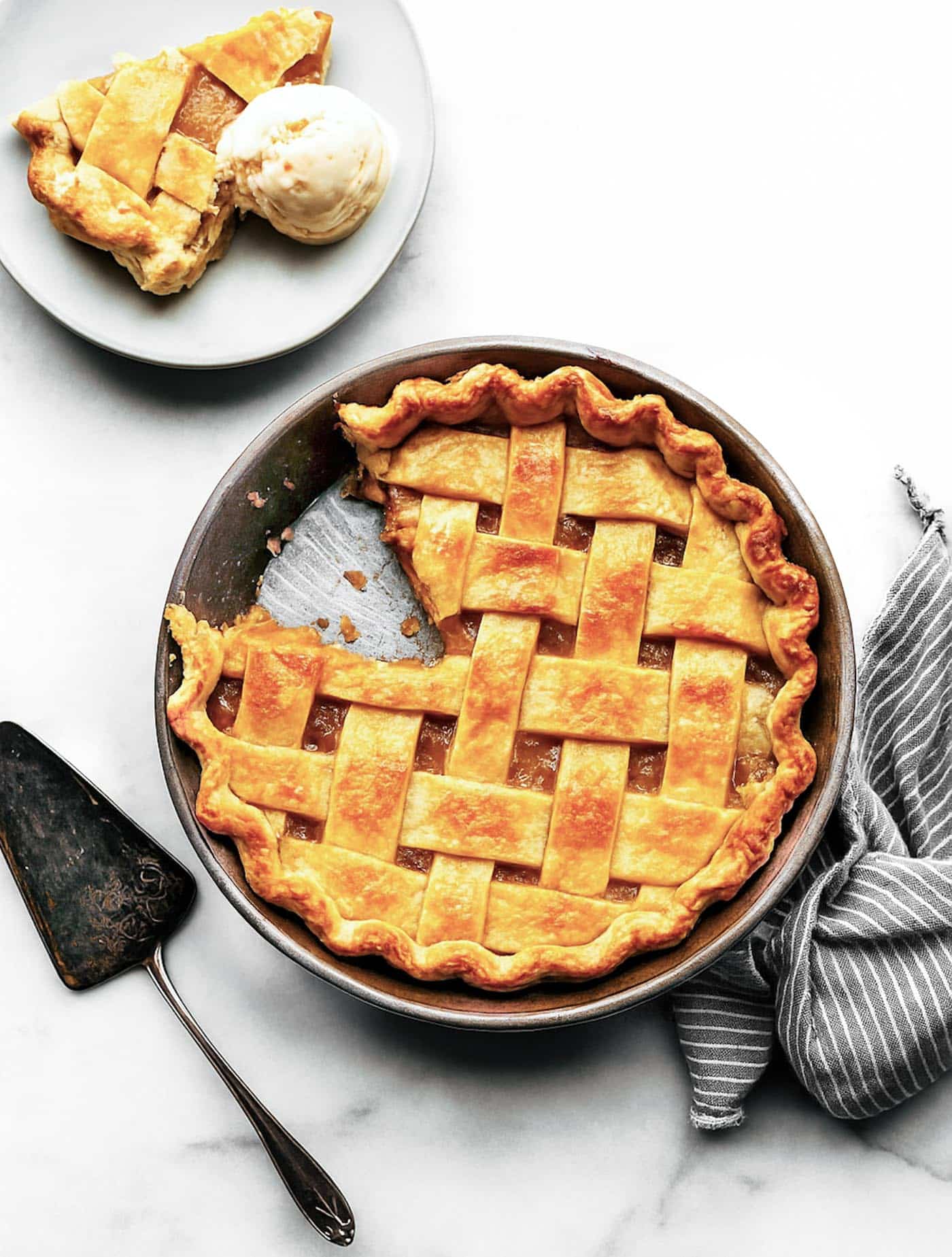 Apricot pie with a slice removed and served on a plate with a scoop of ice cream; a pie server rests beside the pie.