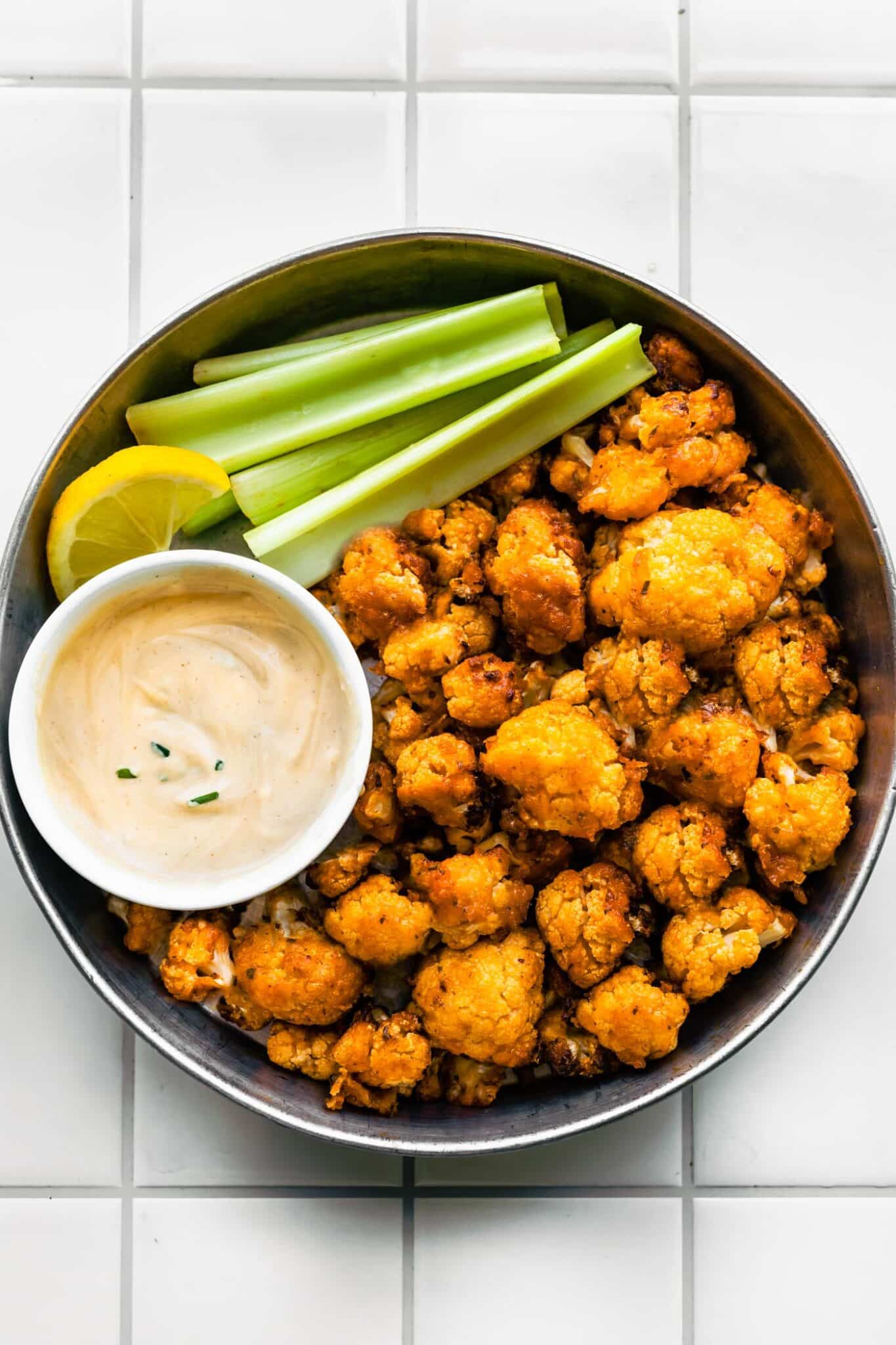 Overhead photo of vegan buffalo cauliflower in a serving dish with celery and dip.