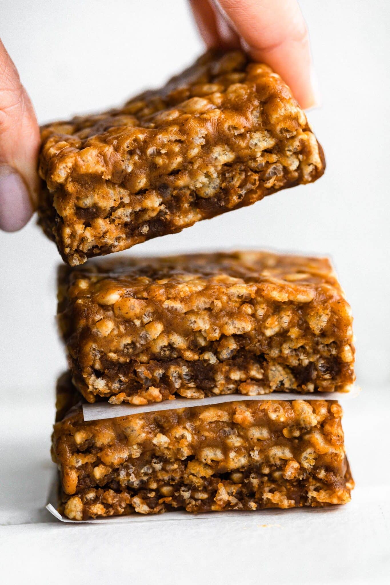 A woman's hand lifting the top protein bar from the stack of three bars.