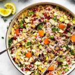 Instant Pot Rice Pilaf with Orzo being stirred in lare serving bowl with garnishes, 2 spoons in middle and lemon wedge on side