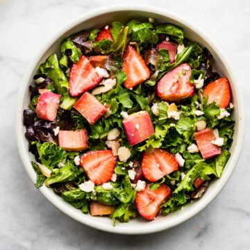 a white bowl filled with strawberry rhubarb salad on marble backdrop