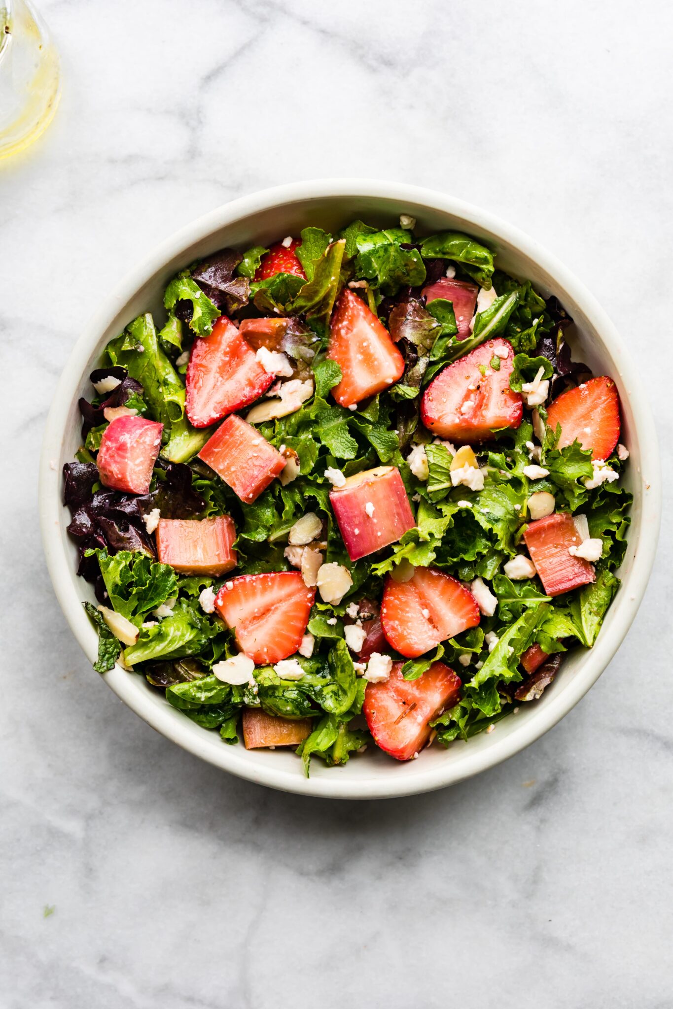 a white bowl filled with strawberry rhubarb salad on marble backdrop