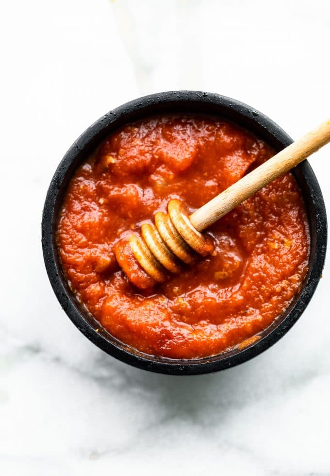 Honey sriracha sauce in small black bowl with honey dipping in sauce.