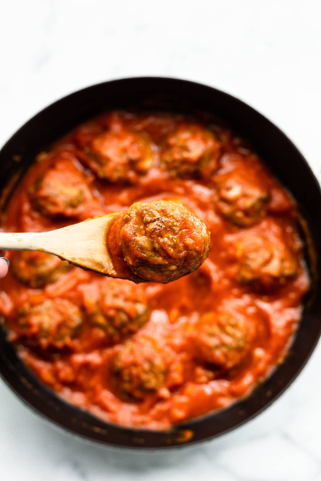 Overhead image of a spoon lifting a turkey meatball from a skillet with sauce.