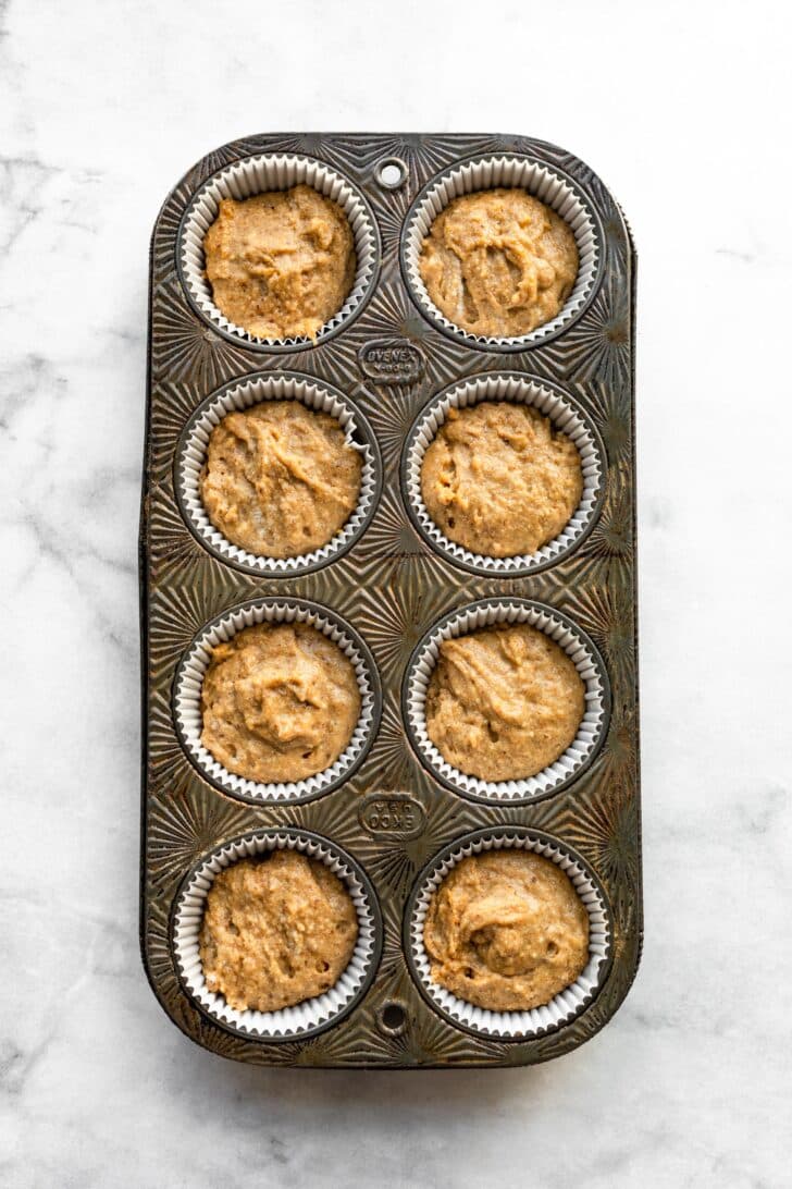 Muffin batter in paper liners in a vintage muffin pan.