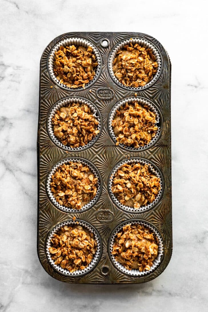 Unbaked muffins with a crumble topping in a vintage muffin pan.