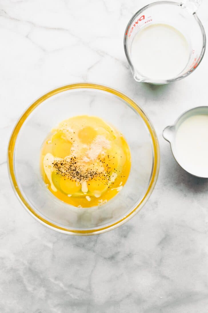 A bowl of eggs topped with black pepper and salt with milk beside it.