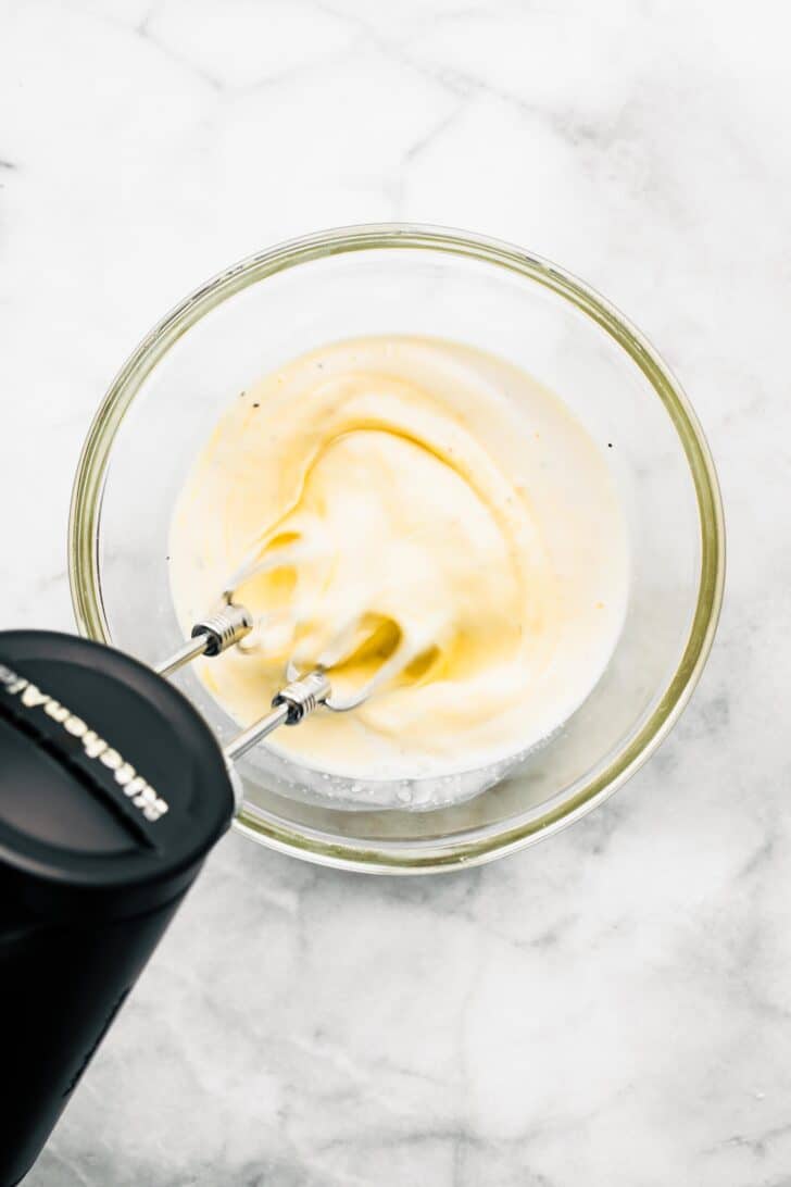 Overhead photo of a hand mixer whisking eggs and milk in a bowl.