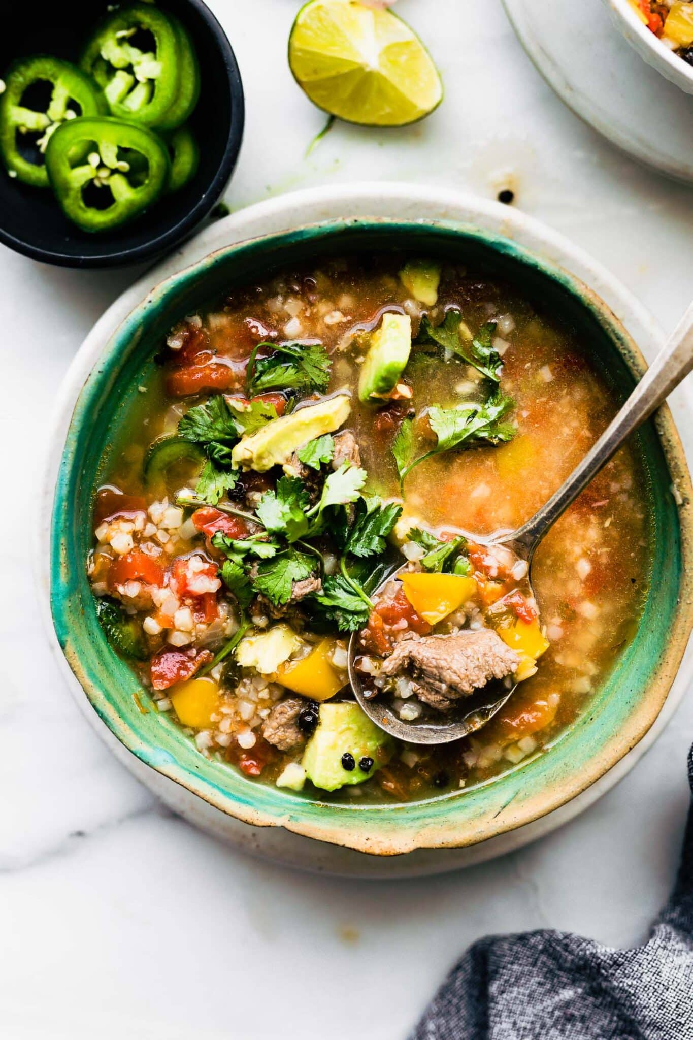 Overhead photo of a homemade ceramic bowl with fajita steak soup and a spoon.