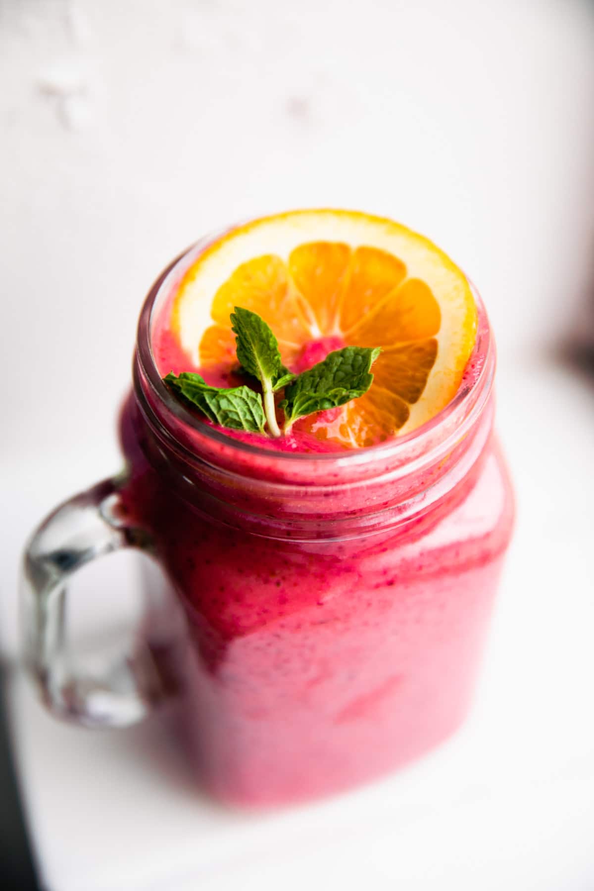 Immunity Boosting Frozen Fruit Smoothie in glass cup topped with fresh orange slice and fresh mint.