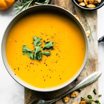 butternut squash soup surrounded by pumpkins, thyme, roasted pumpkin seeds, and a spoon