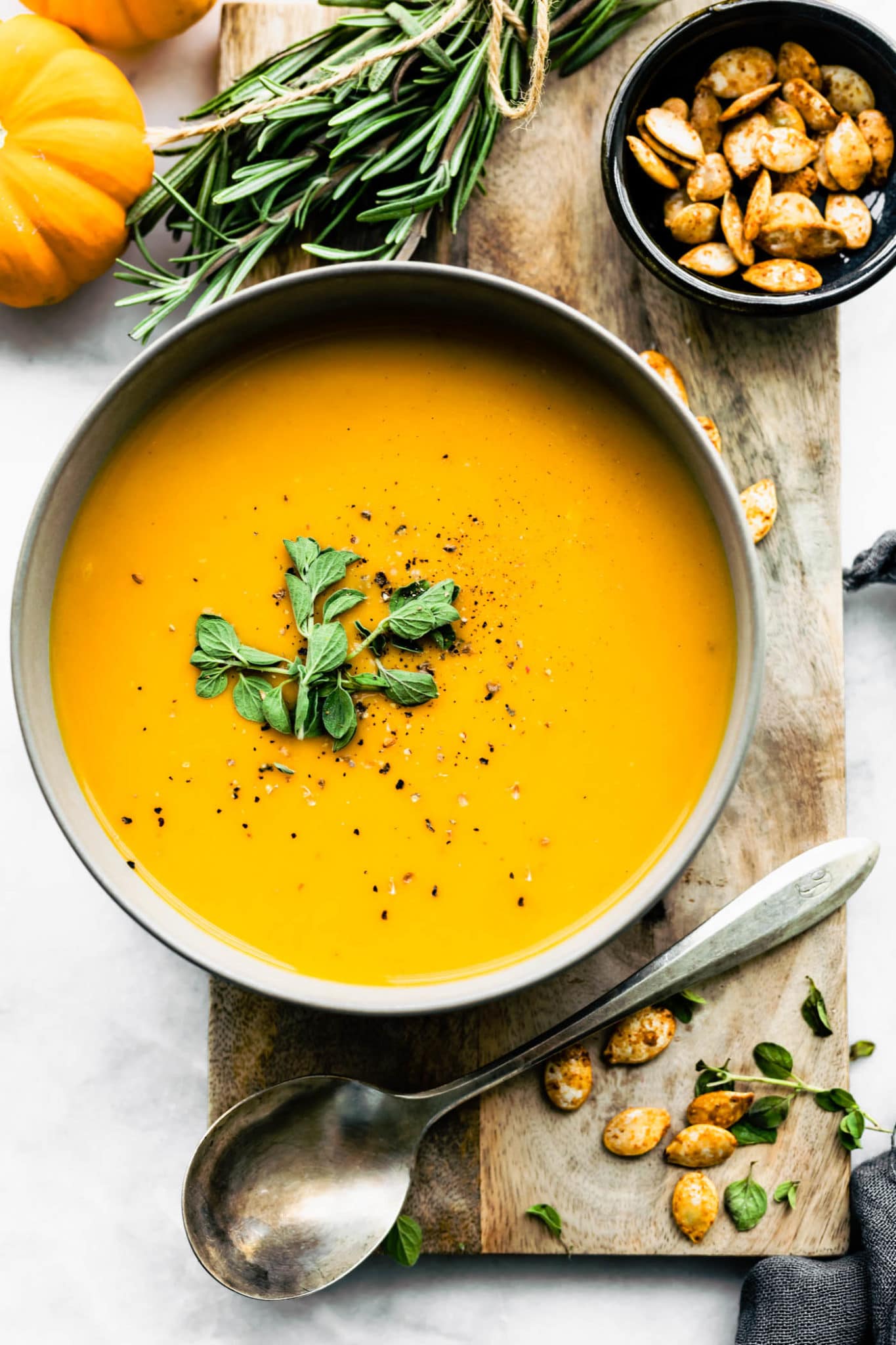 butternut squash soup surrounded by pumpkins, thyme, roasted pumpkin seeds, and a spoon