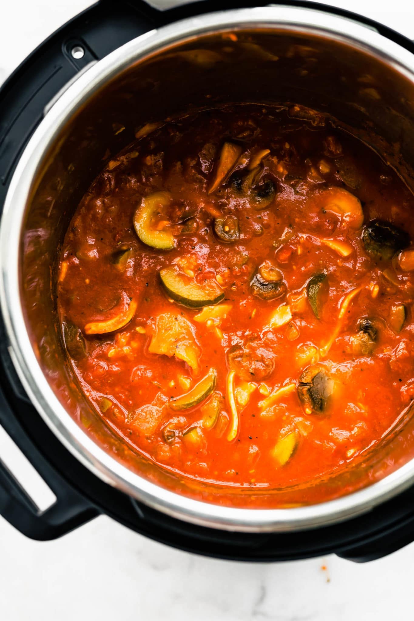 mushrooms and other veggies in an instant pot covered with tomato sauce