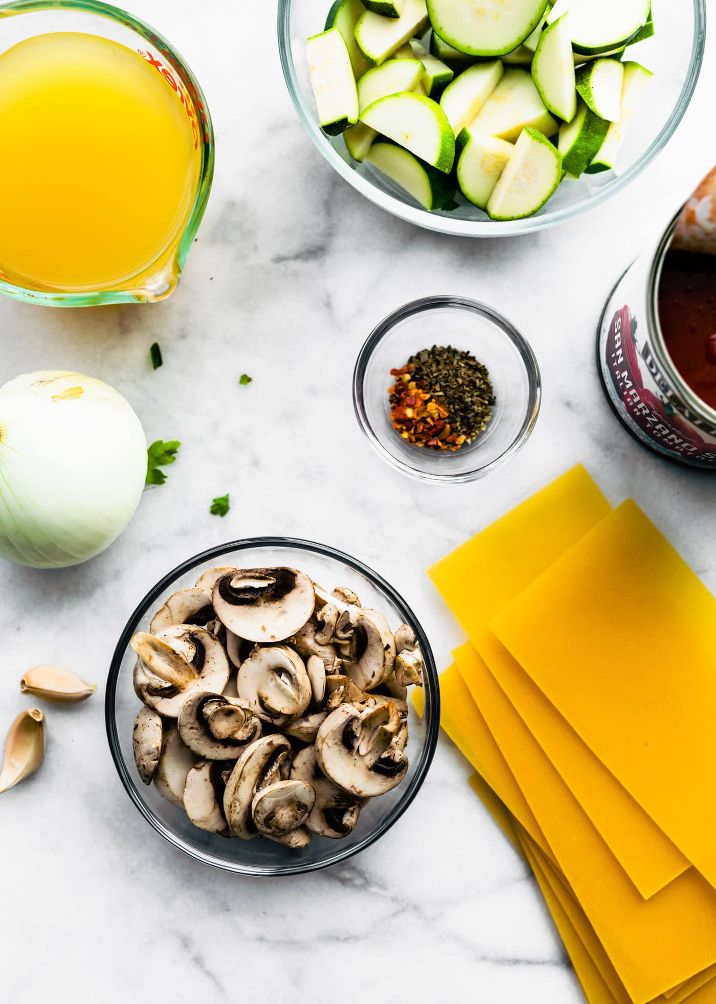 gluten free lasagna noodles, mushrooms, garlic, onion, broth, zucchini, crushed tomatoes, and spices for gluten free lasagna noodle soup on a counter