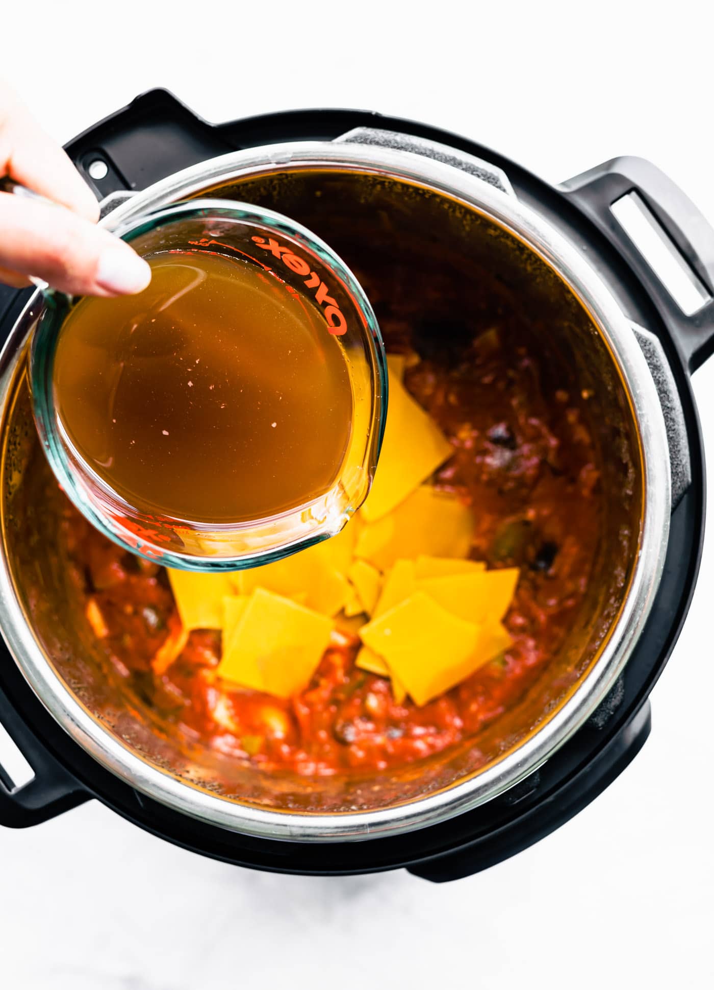 broth being poured over lasagna noodles and and tomato sauce in instant pot