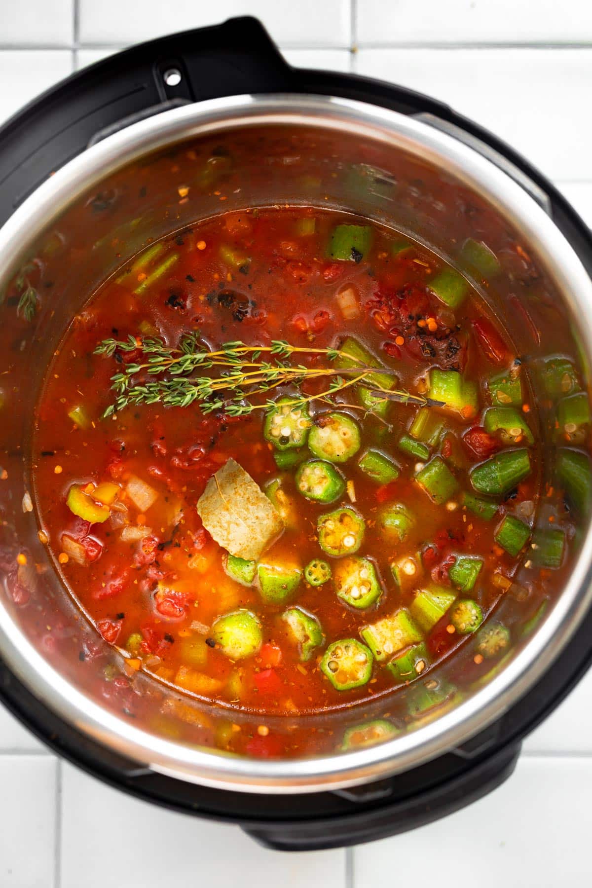 Overhead shot of sautéd ingredients covered in apple cider vinegar, lentils, broth, tomatoes, and hot sauce in an Instant Pot.