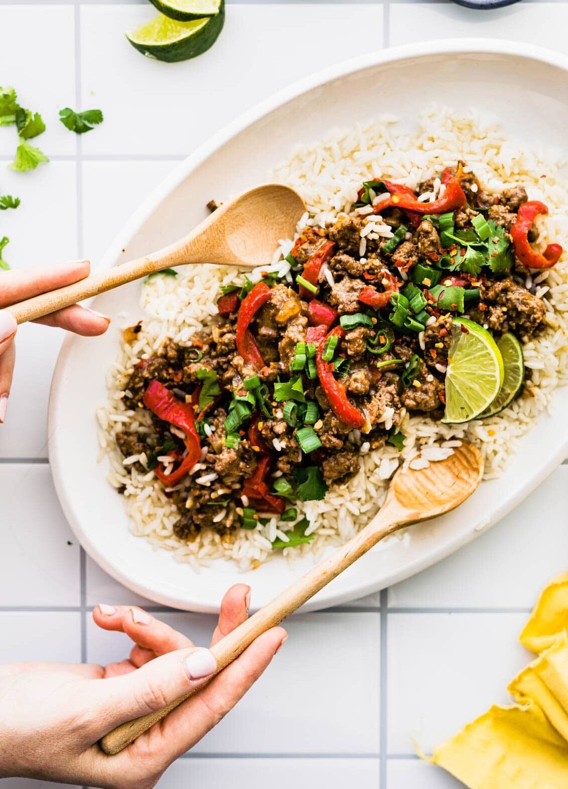 White platter of Korean beef bulgogi over white rice with two wooden spoons for serving.