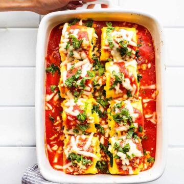 Overhead image of prepared keto egg lasagna roll ups in casserole dish covered in tomato sauce, cheese, and herbs
