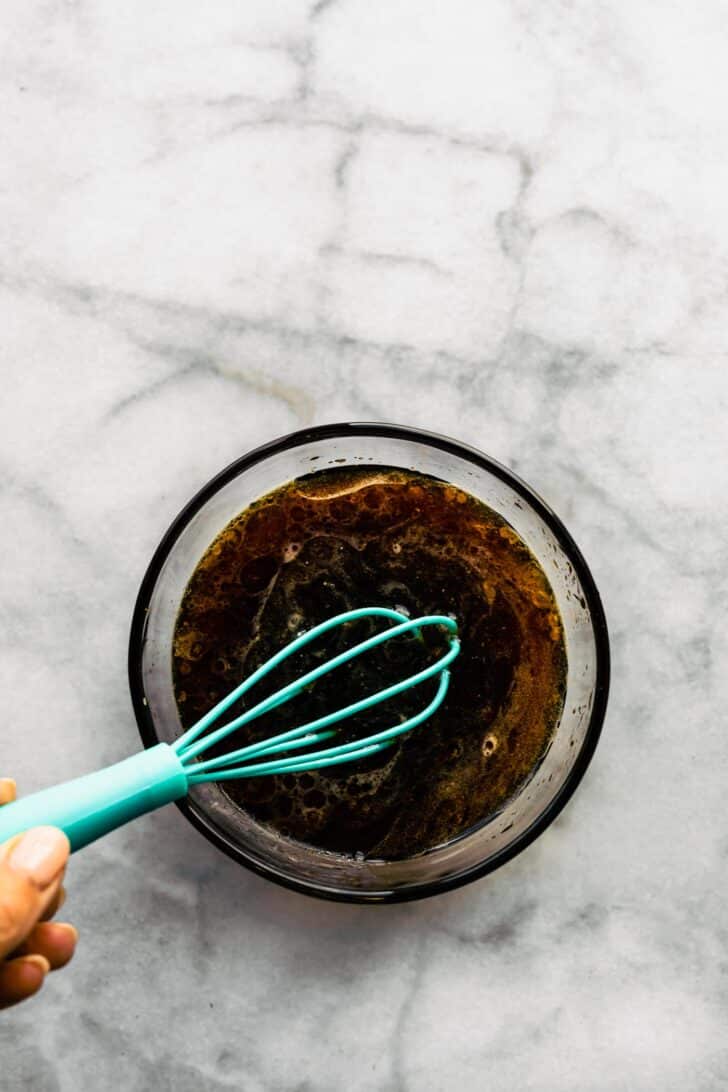 A teal whisk in a glass bowl with Korean sauce for bulgogi.